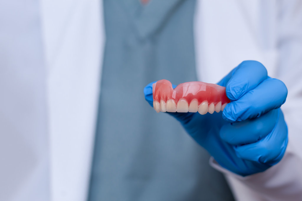 Close-up of a dentist's hand holding a removable full upper jaw denture. Concept of dentistry, oral health, oral rehabilitation, and prosthetic treatment.
