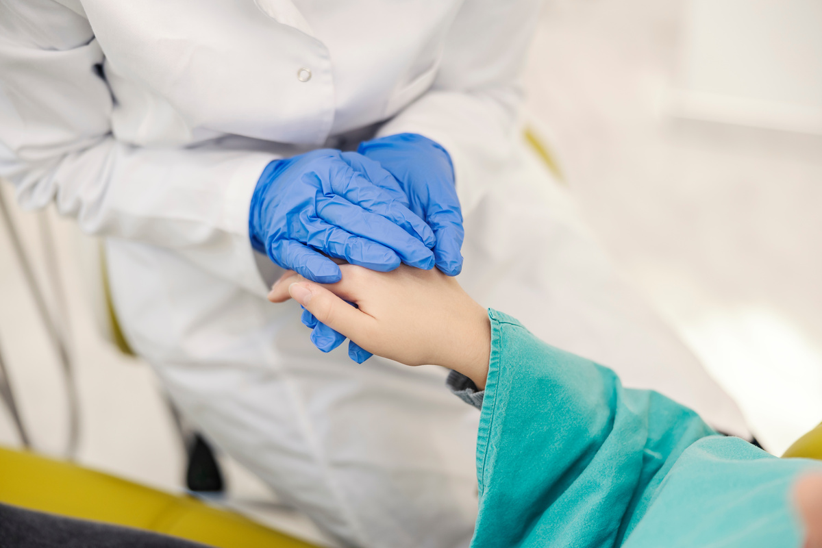 Close up of dentist's hands holding girl's hand at dentist office and comforting a girl.