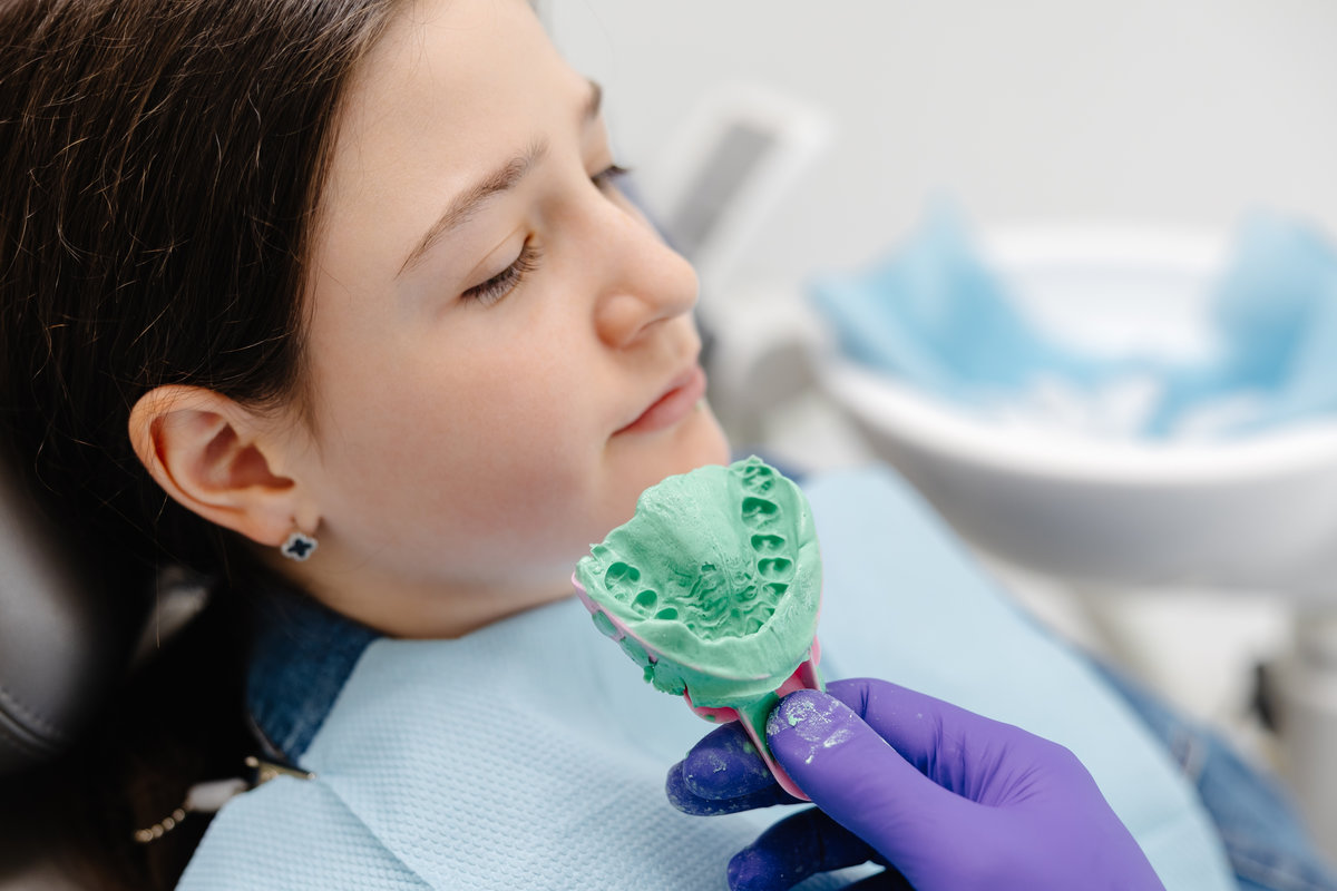 Dentist wearing purple gloves is holding a dental mold of a young patient in a modern dental clinic, ensuring quality oral care
