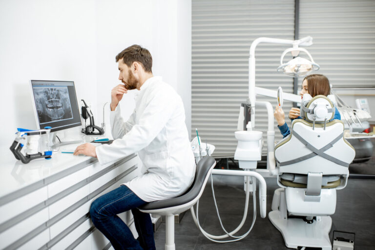 Dentist working with computer in the dental office with woman patient on the background