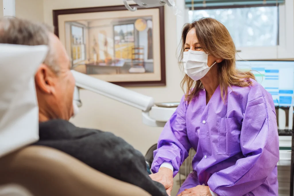 Dental hygienist in purple gloves speaking with senior patient in treatment room