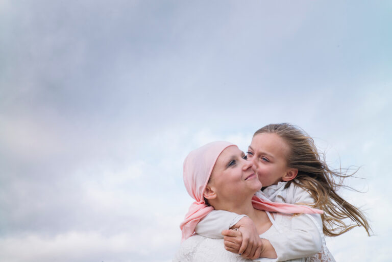 A woman with cancer is next to her daughter. A girl is hugging a woman happy